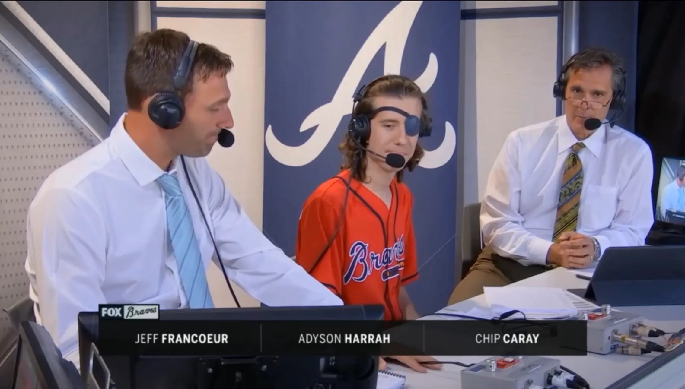 Adyson Harrah in the Atlanta Braves broadcast booth between Jeff Francoeur and Chip Caray, lower-third graphic identifying all three on air.